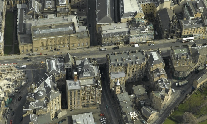 view from a plane or helicopter down onto a road which runs across the screen from left to right, suspended halfway up the buildings around it with other streets passing through tunnels underneath it