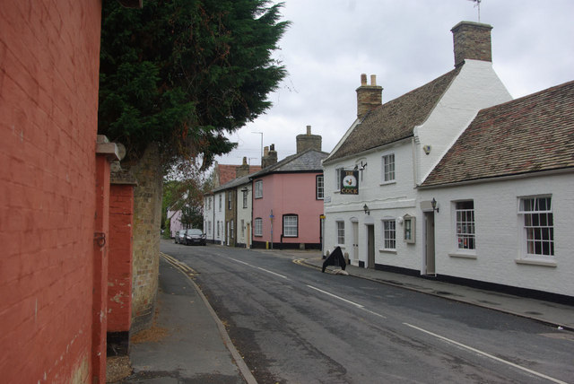 village street of small old-fashioned buildings in white, brown and pink, including a white pub