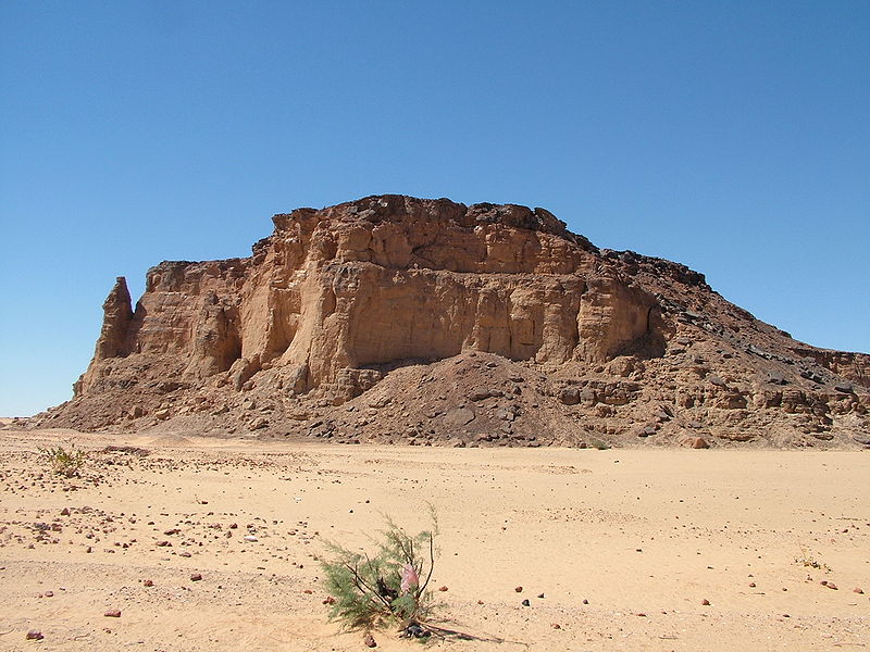 hill of rugged, worn sandstone rising abruptly from a sandy plain