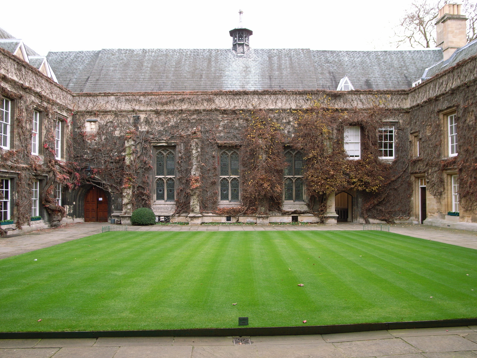 two-storey, ivy-covered stone buildings with ornate windows, surrounding a stripey lawn