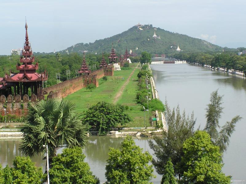 artificial waterway crossing the foreground and then turning at right-angles to stretch away along the right of the picture towards a distant conical hill, with a stretch of grass along the left side and a low wall puntuated with small raspberry-pink pagodas