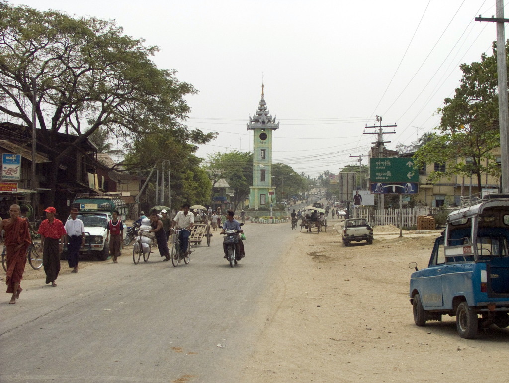 view of a wide dusty street leading towards a tall white tower with a pagoda roof