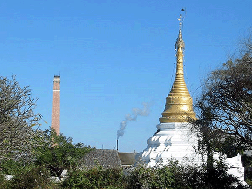 to the right of the picture a broad white conical building culminating in a tapering golden spire, the whole rather resembling an upended ice-cream cone, surrounded by trees, with a tall thin oblong tan brick tower in the background on the left