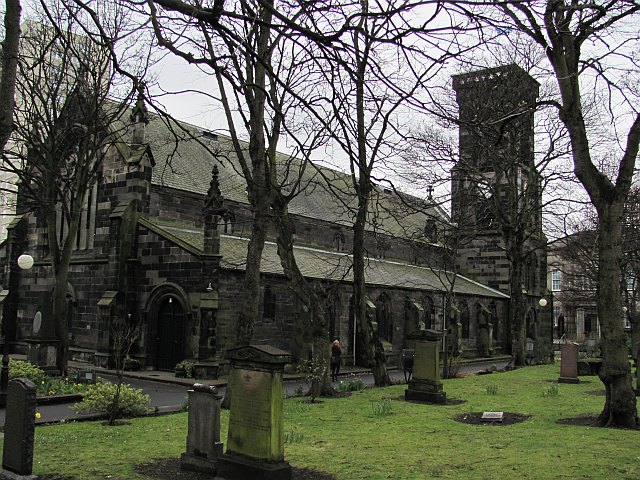 large, long, dark stone church with a double slope of roof and a square tower to the right, surrounded by gravestones and bare trees