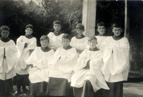 greyscale photo\' showing three seated boys and six standing in a row behind them, all in white surplices over dark gowns