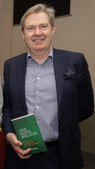 Photo\' of smiling middle-aged man in dark suit, holding a book