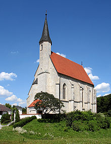 small whitewashed church with little buttresses along the sides, a steep red roof and a bell-tower tipped with a dark conical spire, standing on a green mound covered with bushes