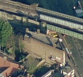 slanted aerial view of skewed-looking brown building with a white front, next to a railway line